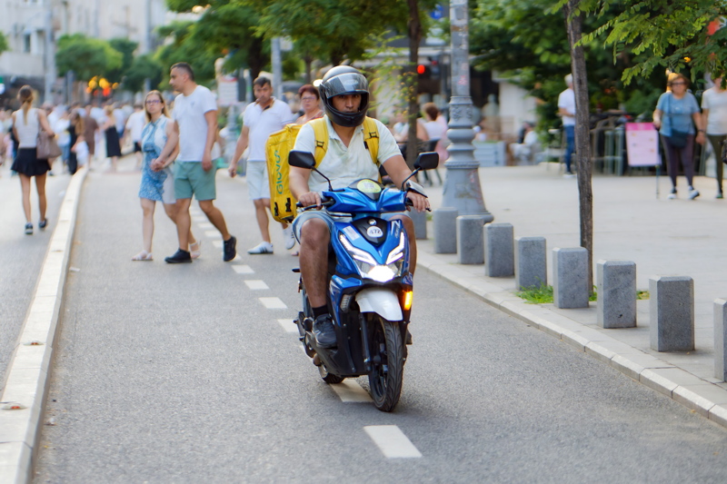 30 - A Glovo food delivery rider operating a blue scooter on a city street